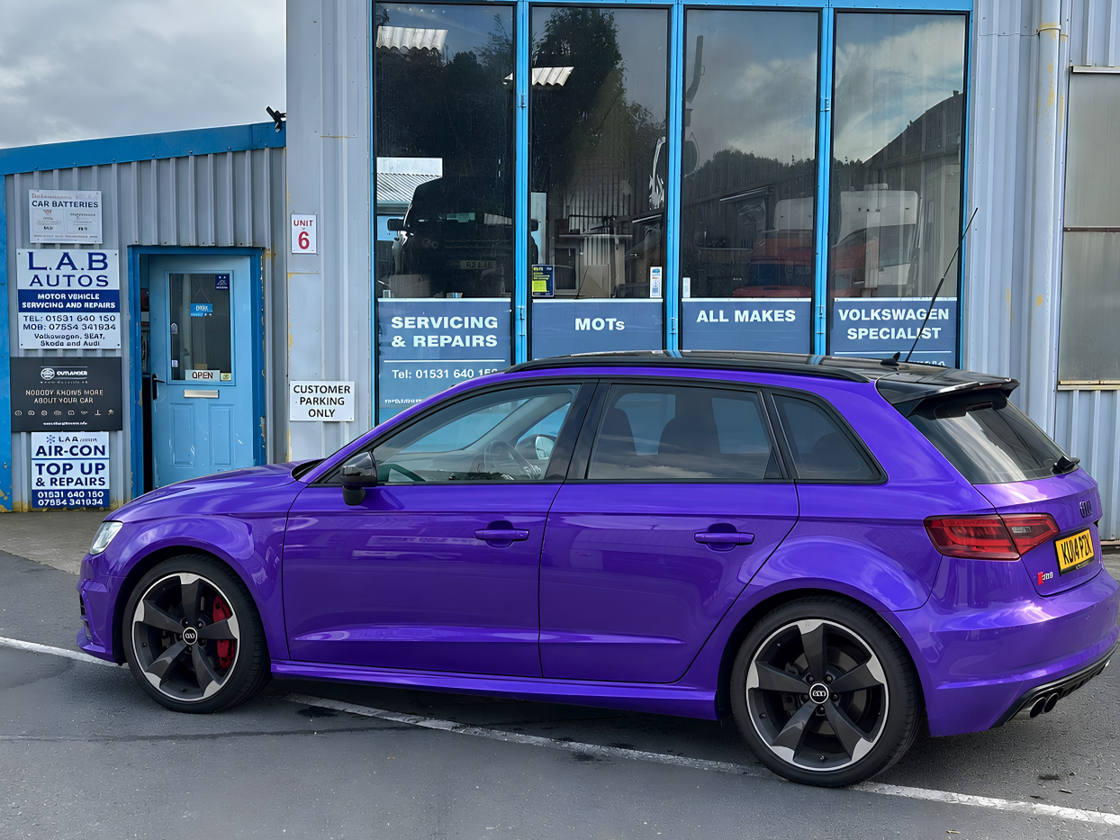 A technician connects a Hella Gutmann diagnostic tool to an Audi S3 to fix a persistent lighting fault.